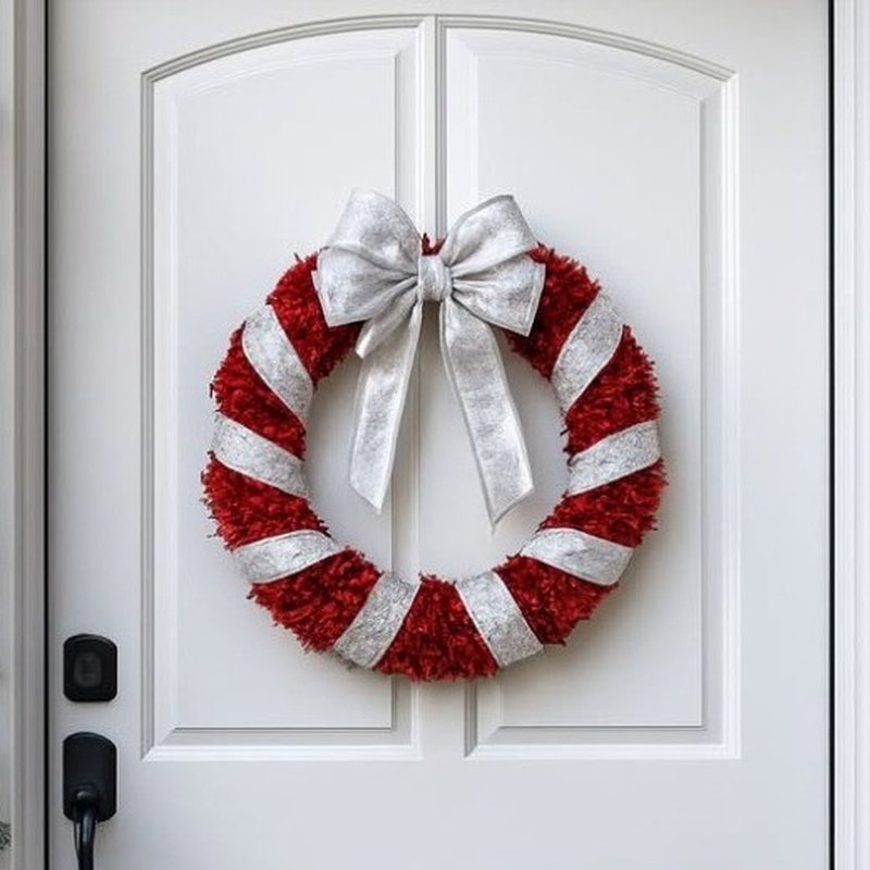 Red and silver candy cane tinsel wreath with a large silver bow on a white door